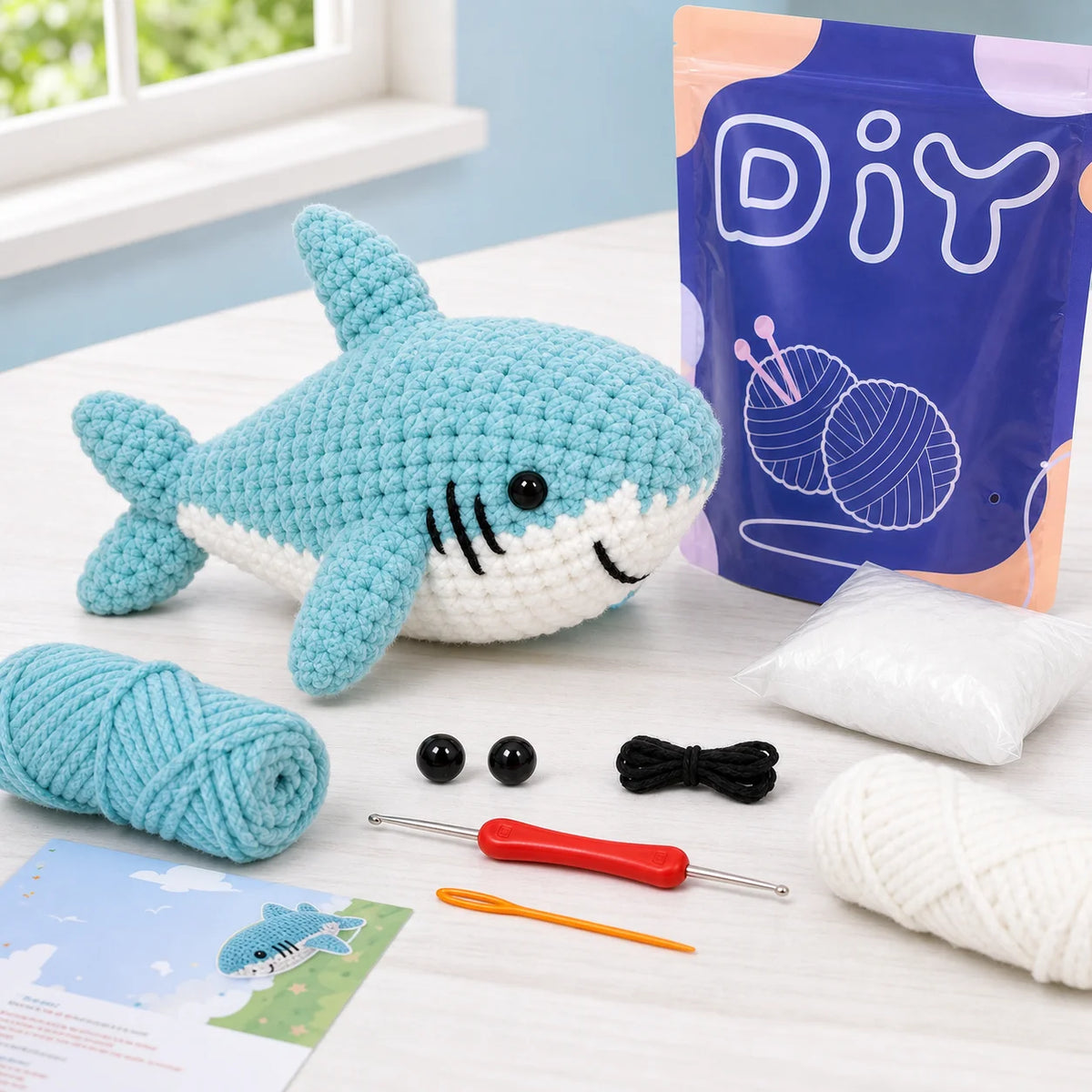 A beginner crochet kit featuring a blue shark amigurumi, yarn, and tools on a white surface.