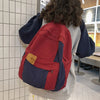 A person is wearing a red and navy canvas patchwork backpack while standing in a modern indoor space.