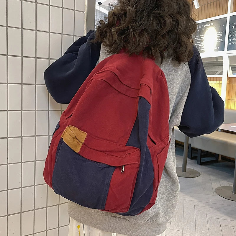 A person is wearing a red and navy canvas patchwork backpack while standing in a modern indoor space.