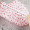 A translucent pink disposable waterproof shower cap with white elastic bands and pink polka dots.