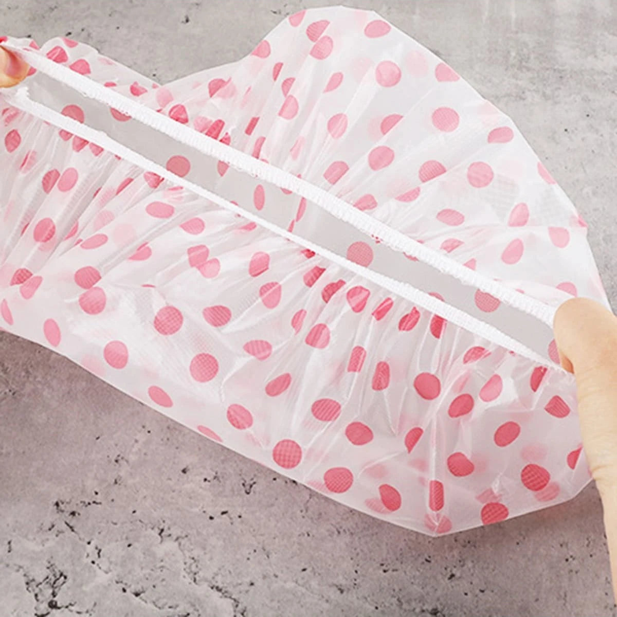 A translucent pink disposable waterproof shower cap with white elastic bands and pink polka dots.