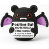 A handmade black crochet bat doll with purple accents and a positive message card.