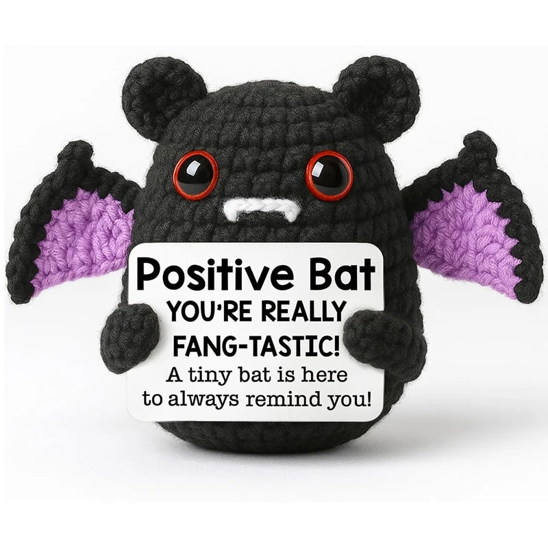 A handmade black crochet bat doll with purple accents and a positive message card.
