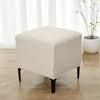 A beige geometric jacquard stretch ottoman cover placed on a wooden floor near a window.
