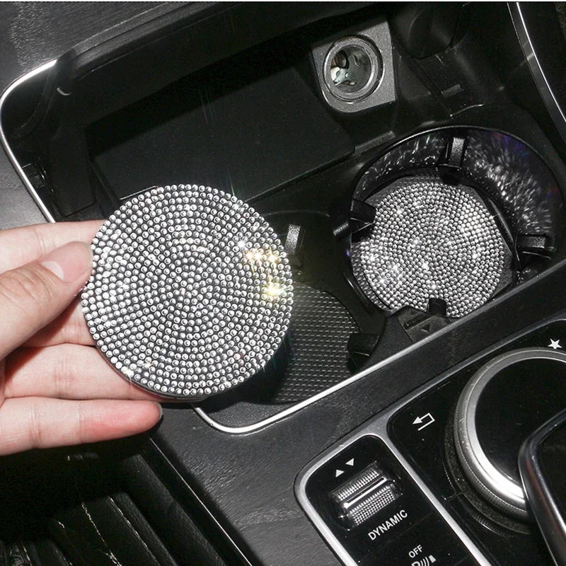 A hand holds a round, silver diamond-encrusted coaster, showing its texture and sparkle inside a car cup holder.