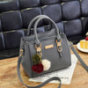 A gray vintage PU leather shoulder bag with gold hardware and a fluffy pom-pom charm resting on a wooden surface.