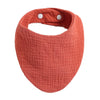 A terracotta orange organic cotton muslin baby bib with an absorbent bandana and a loop for fastening.