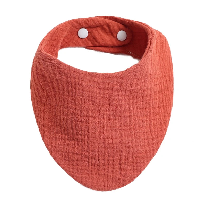 A terracotta orange organic cotton muslin baby bib with an absorbent bandana and a loop for fastening.