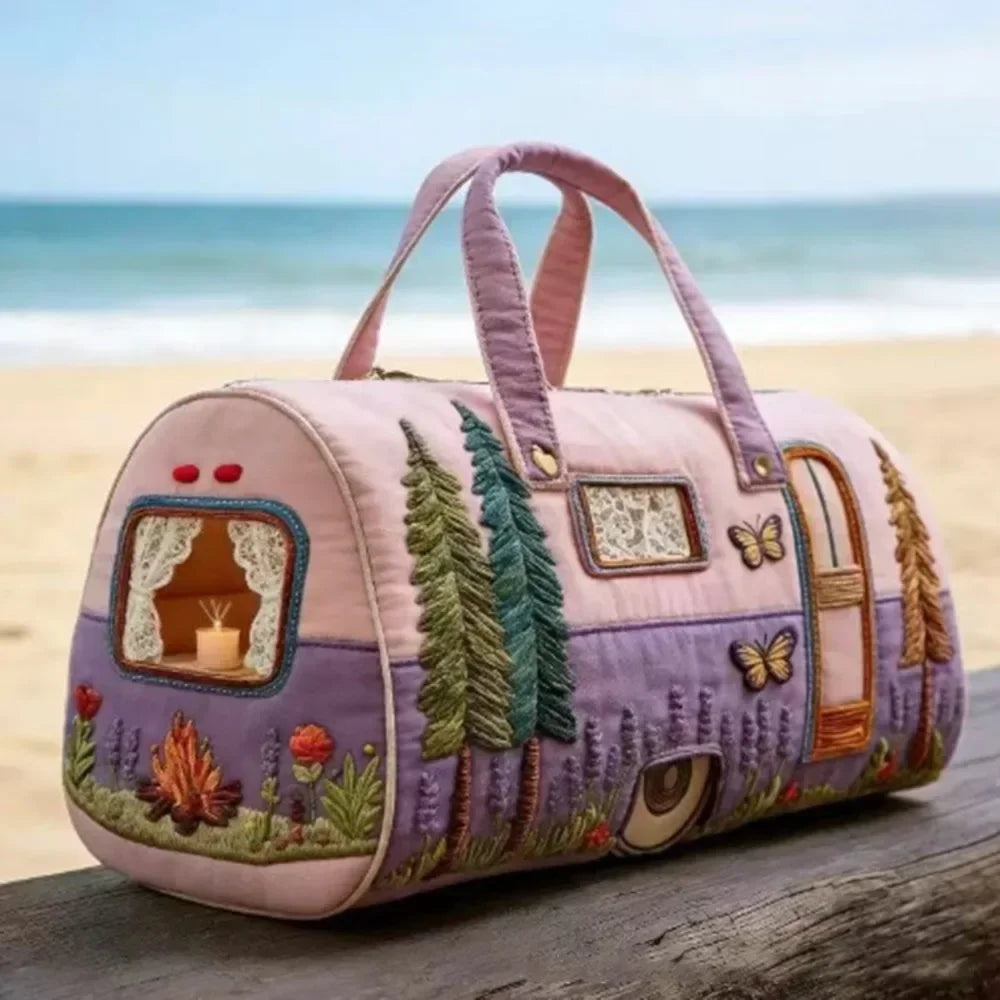 A pink quilted travel duffle bag with purple accents and green foliage stitching resting on a wooden surface.