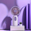 A white mini USB rechargeable handheld fan with a purple grille is displayed on a white surface against a purple background.