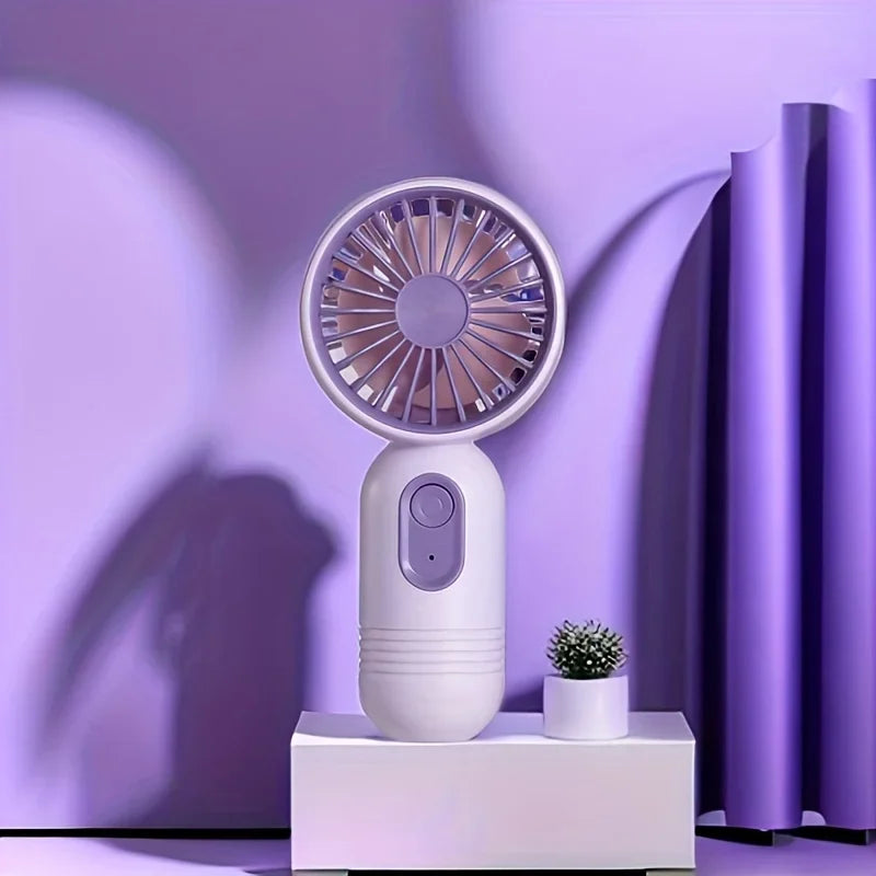 A white mini USB rechargeable handheld fan with a purple grille is displayed on a white surface against a purple background.