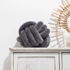 A dark gray, hand-knotted velvet decorative cushion resting on a white wooden shelf.