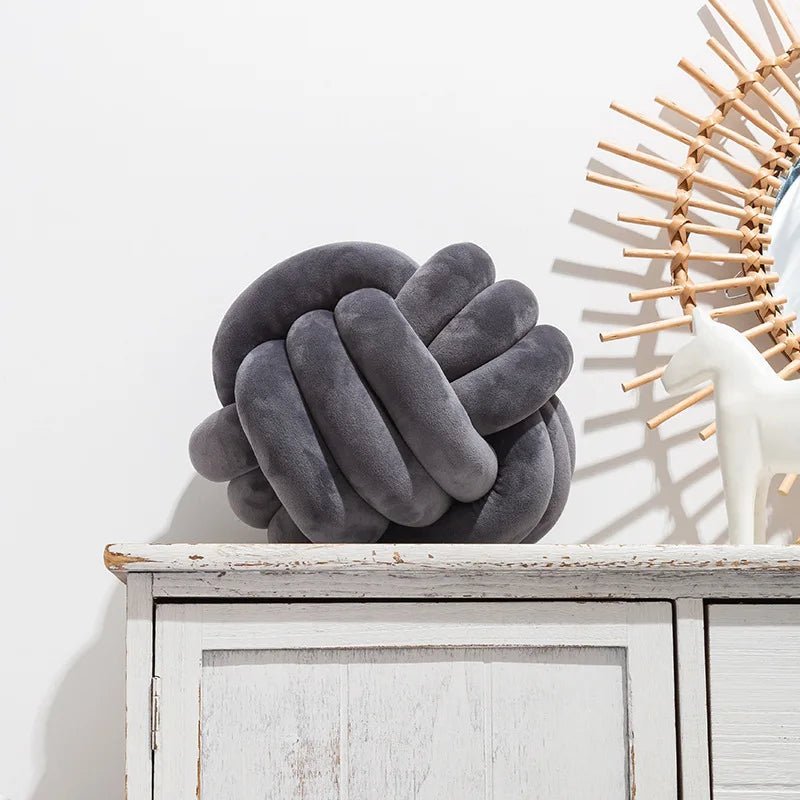 A dark gray, hand-knotted velvet decorative cushion resting on a white wooden shelf.