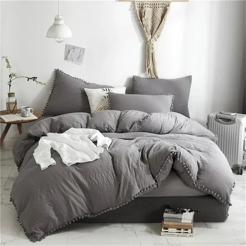 A gray duvet cover set with pom tassels and white accents displayed on a bed.