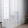 White sheer voile curtain panel with delicate silver embroidery hanging in a window.