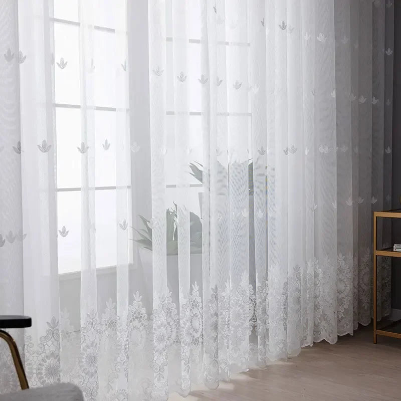 White sheer voile curtain panel with delicate silver embroidery hanging in a window.