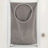 A gray laundry storage bag with a circular opening is hanging on a white door.