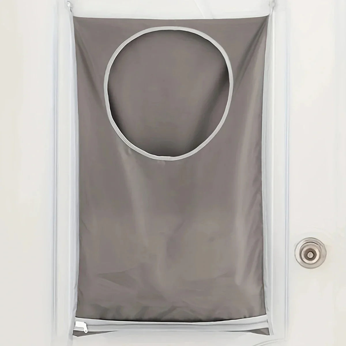 A gray laundry storage bag with a circular opening is hanging on a white door.