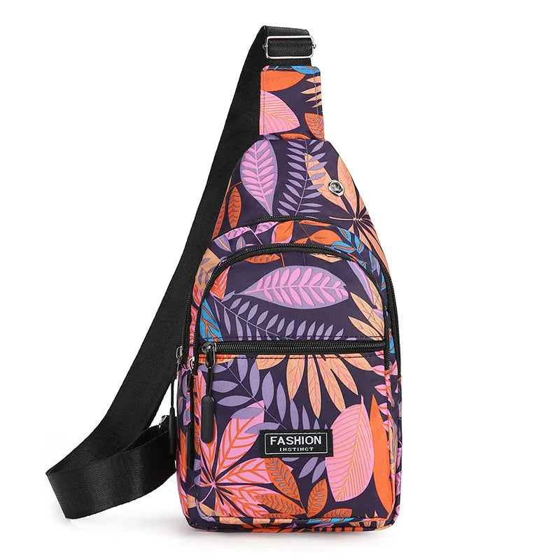 A purple and orange leaf print sling crossbody bag with a black strap and multiple zippered pockets.