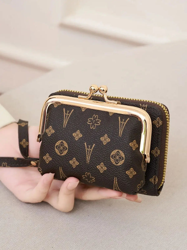A dark brown patterned accordion wallet with a gold-toned metal clasp and a black wristlet strap is held in a person's hand.