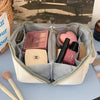 A beige cosmetic storage bag with a zipper, containing various makeup products and tools.