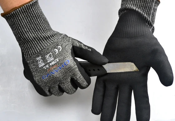 A hand wearing black cut-resistant work gloves holding a silver utility knife.