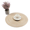 A round woven placemat with a white cup and saucer, next to a potted purple plant.