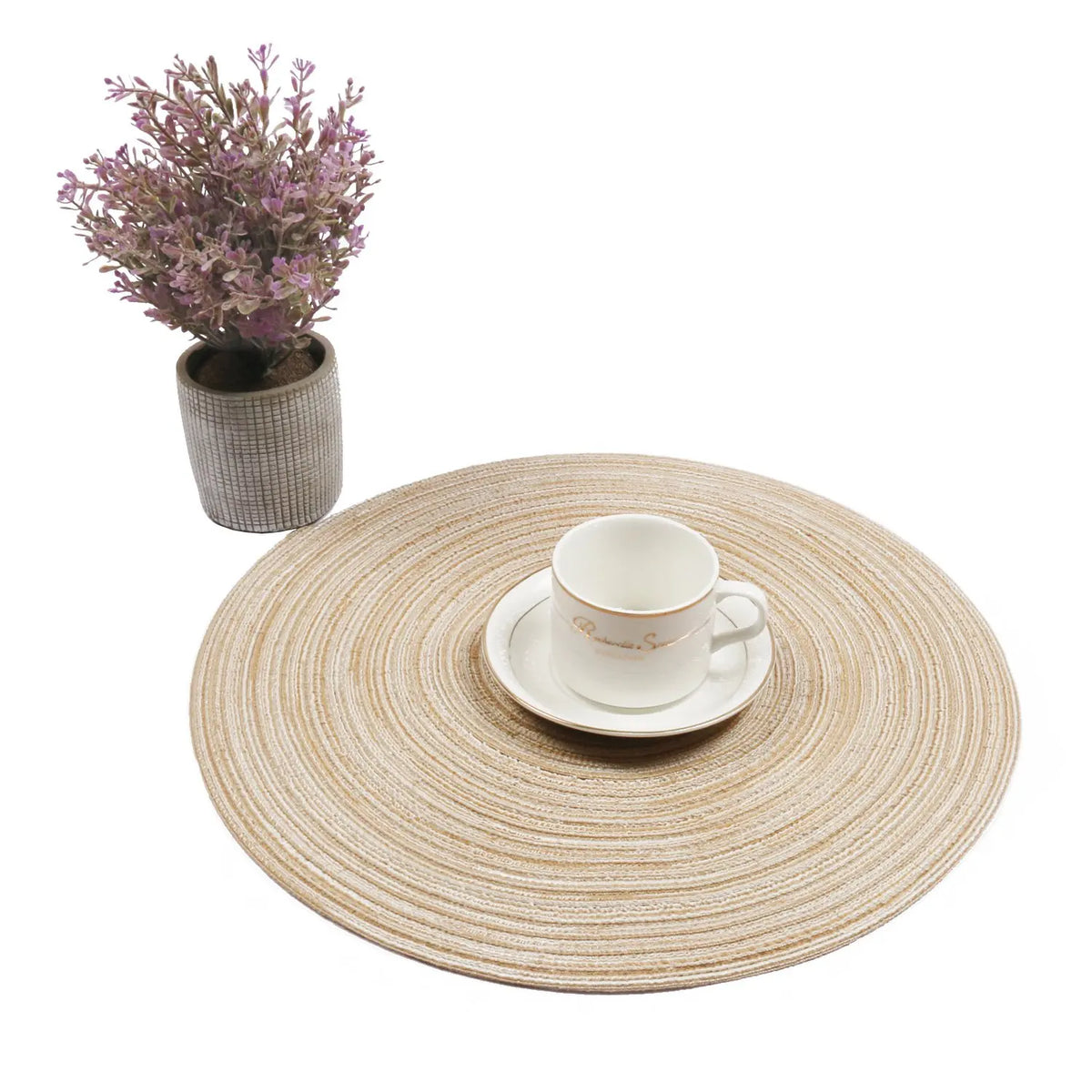 A round woven placemat with a white cup and saucer, next to a potted purple plant.