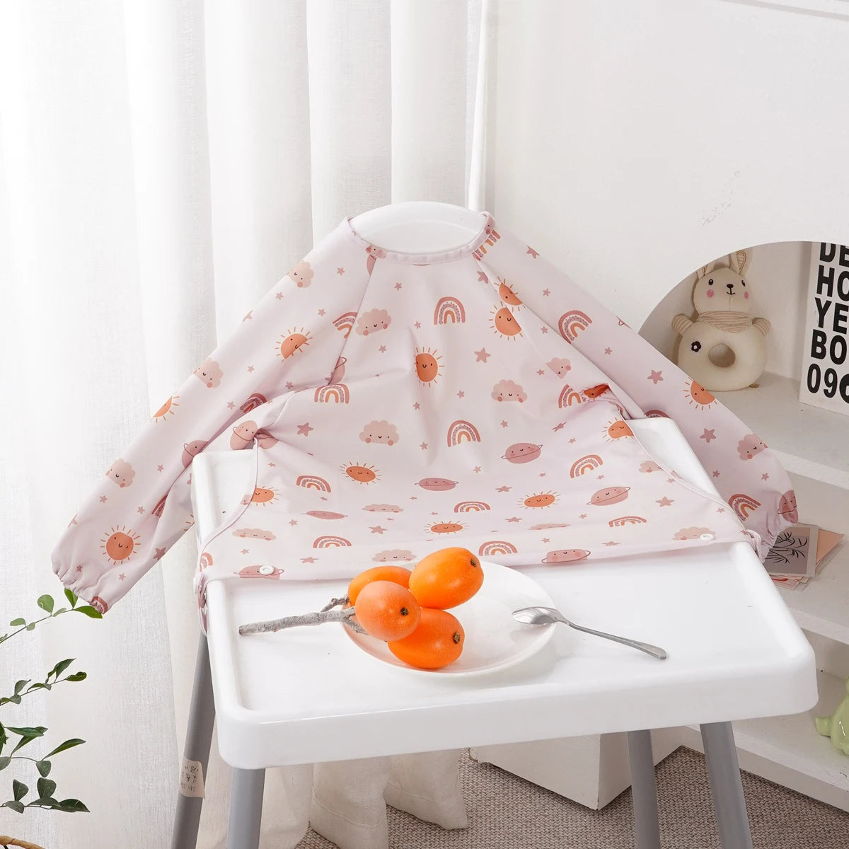 Pink long-sleeve waterproof baby bibs with a cute animal design displayed on a white table.
