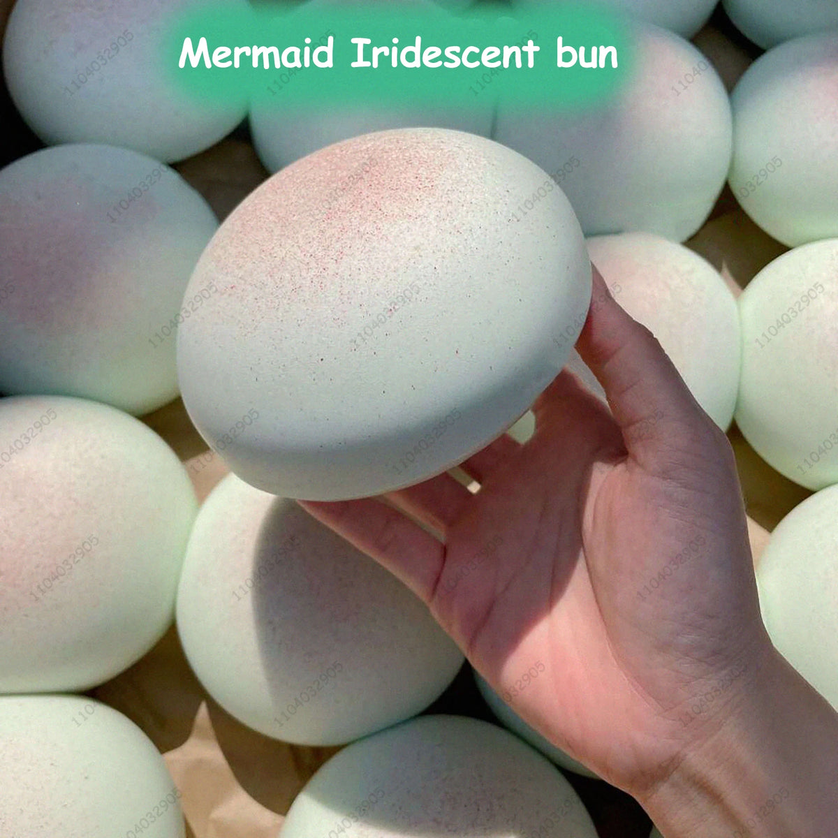 A hand holds a round, white, iridescent bun squishy against a background of similar items.