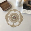 An elegant oval lace embroidered placemat with floral details rests on a white surface next to a wooden tray and a ceramic cu
