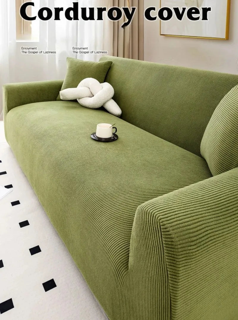 A textured olive green stretch jacquard sofa cover with a white decorative pillow and a cup on the cushion.