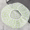 A white disposable waterproof shower cap with light green polka dots is shown on a dark gray surface.
