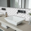 A modern white vessel sink installed on a light wood countertop with a subway tile backsplash and black faucet.