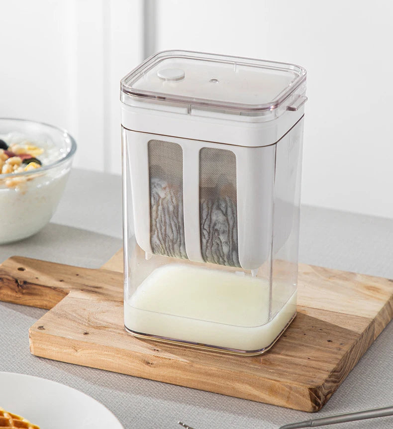 A clear plastic yogurt strainer with a fine mesh filter is placed on a wooden cutting board.