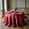 An elegant round table set with a deep red satin tablecloth, white plates, and floral centerpiece.