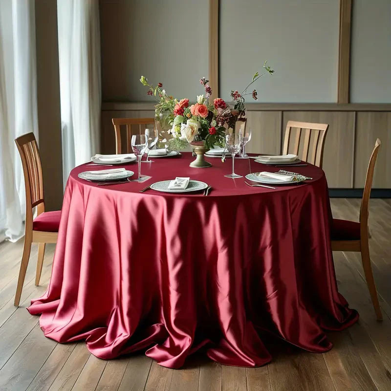 An elegant round table set with a deep red satin tablecloth, white plates, and floral centerpiece.
