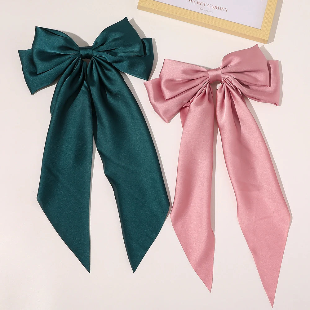 A pair of silk bow hair clips in deep emerald green and dusty rose pink.