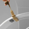 A hand is lifting a beige plastic toilet lid lifter from the rim of a white toilet bowl.