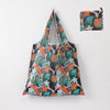 A reusable shopping tote bag featuring a tropical leaf pattern in shades of green, orange, and pink.