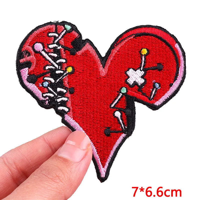 A red heart shaped patch embroidered with various colored pins and needles on a black fabric background.