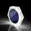 A clear, hexagonal solar-powered LED step and path light with a blue solar panel visible inside.