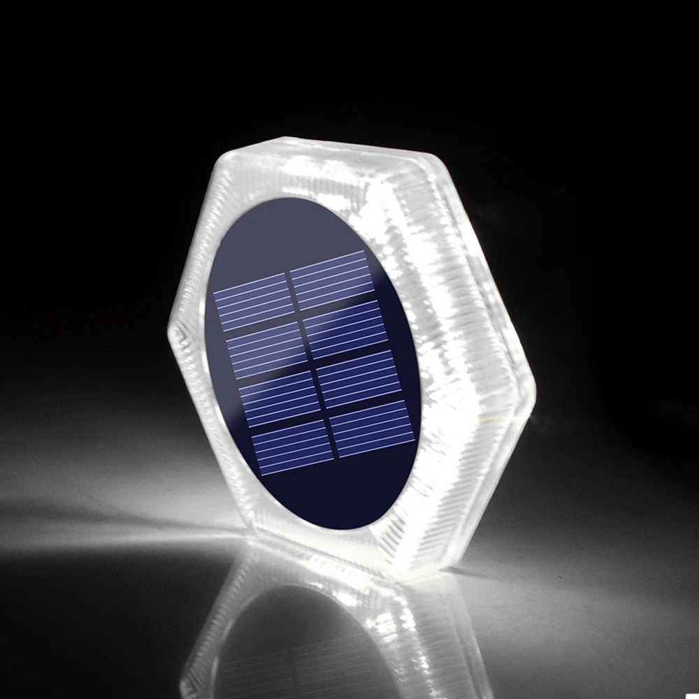A clear, hexagonal solar-powered LED step and path light with a blue solar panel visible inside.