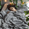 Une femme dort sous une couverture en flanelle grise et moelleuse dans une pièce faiblement éclairée.
