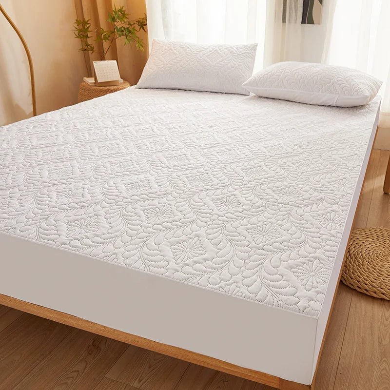 A white quilted mattress protector with extra padding is displayed on a wooden bed frame.