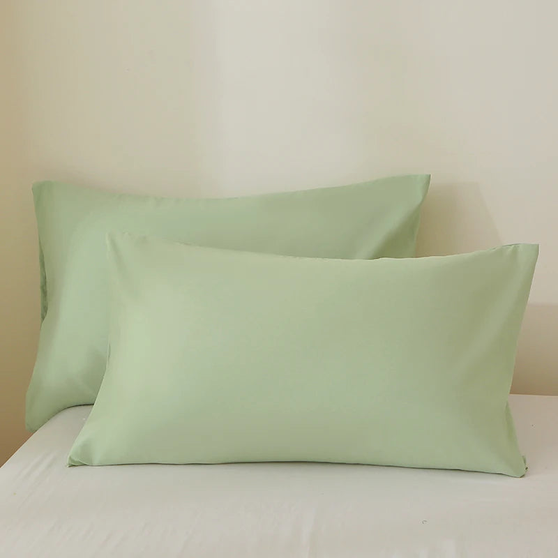 A set of three light sage green pillow covers resting on a white bed.