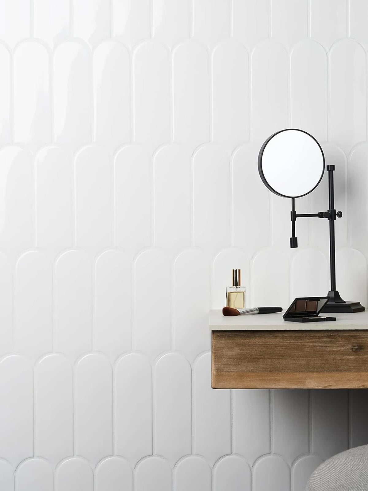 A close-up of a modern bathroom wall featuring white raised tile paneling and a black wall-mounted magnifying mirror.