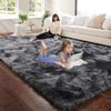 A young girl lies on a dark gray plush carpet in a bright living room with a woman and a dog nearby.
