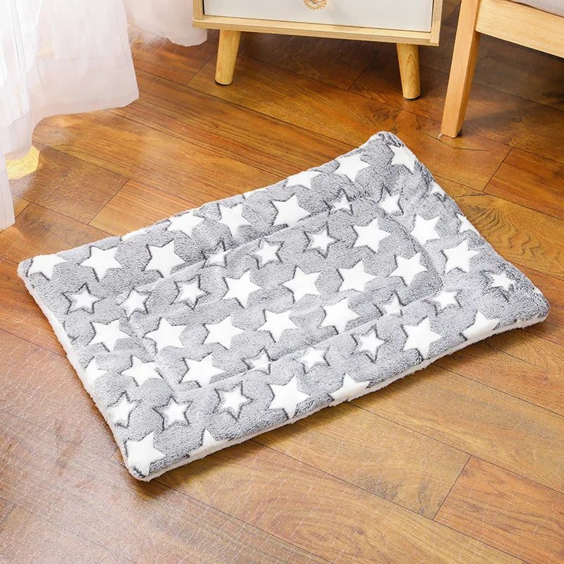 A gray and white star patterned plush pet sleeping mat lying on a wooden floor.