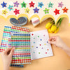 A hand is holding a sheet of glitter star stickers and a piece of lined paper with star designs on a light background.